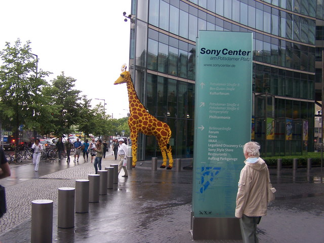 A life-sized model of a giraffe stands in a busy public plaza.